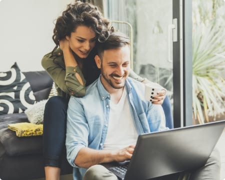 Image d'ilustration montrant un couple cis blanc hétéro souriant devant un ordinateur
