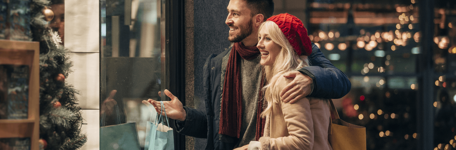 Un employé de Boulanger apportant des produits emballés dans du papier cadeau à un cliente attendant devant son coffre de voiture ouvert
